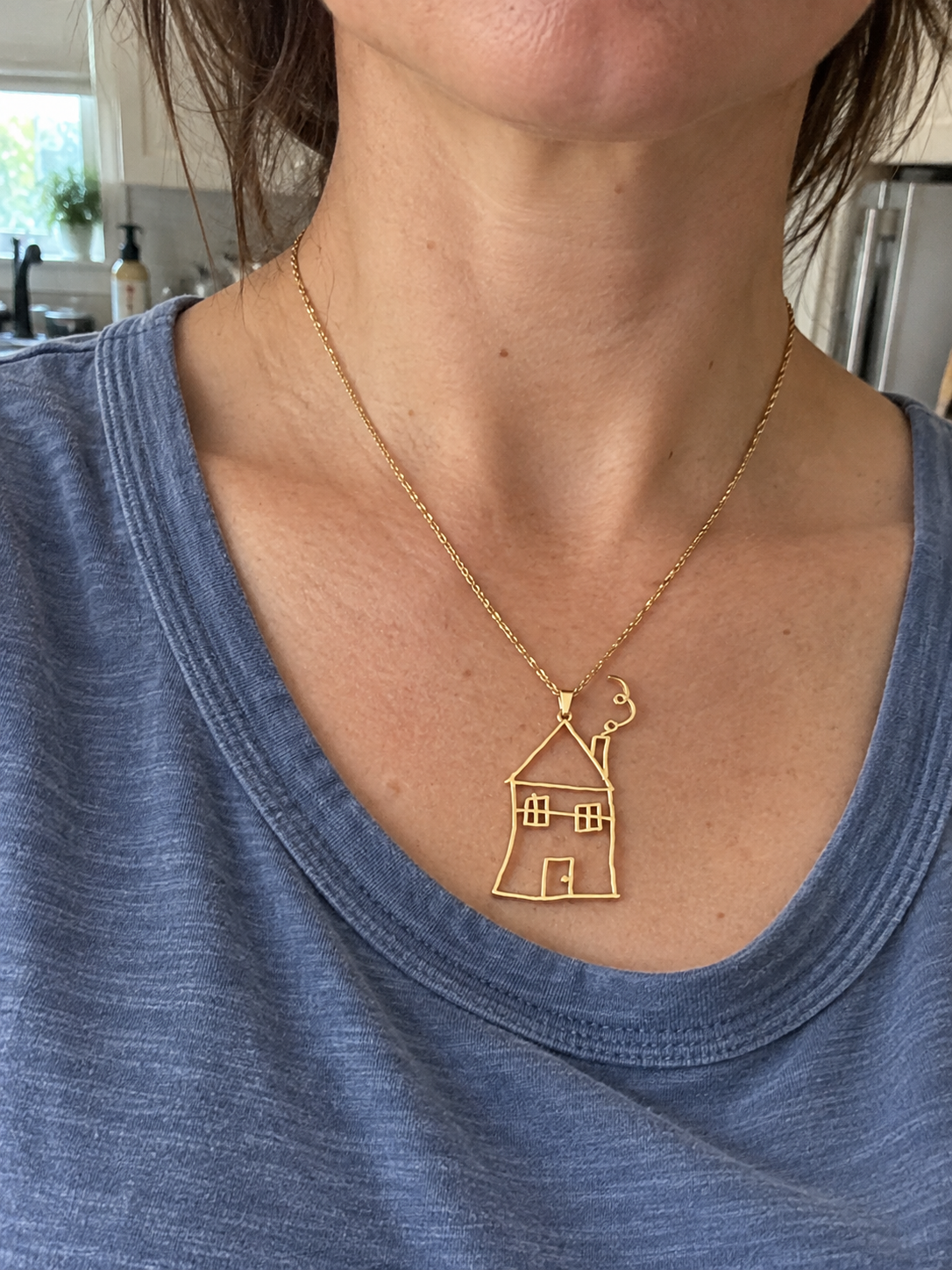The customer wearing the gold house necklace made from her child's drawing